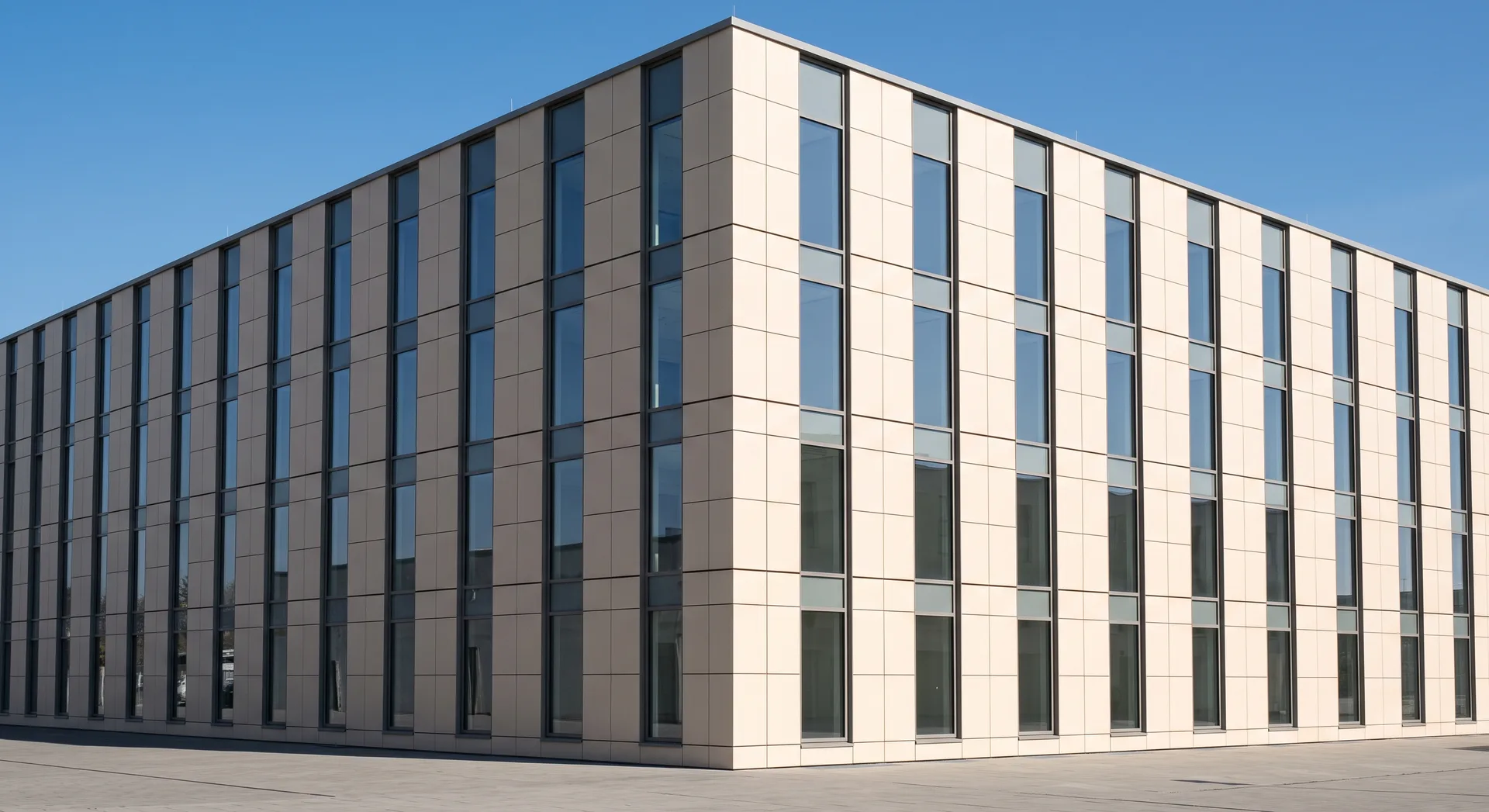 A contemporary building with a pale panelled façade in a precise grid and flush full-height glazing, its flat planes lit hard from one side.